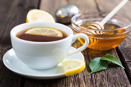 Cup of hot tea with a lemon next to a jar of honey
